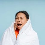 Yawning woman relaxing at home wrapped in soft blanket, feeling tired isolated on blue background studio portrait. Bad nap concept